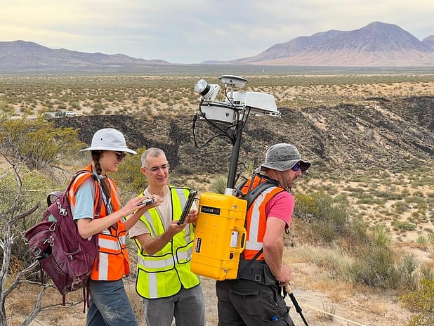 Researchers attach a lidar unit to another's back in the desert.